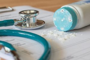 Baby powder product with talc mineral spilling over diagnosis record paper on doctor's pad with stethoscope